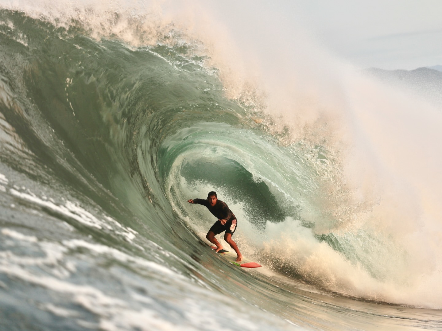 Surfer riding through a green wave barrel